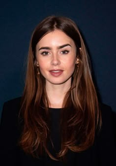 a woman with long brown hair is posing for the camera in front of a dark background