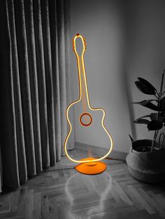 a guitar shaped lamp sitting on top of a hard wood floor next to a potted plant