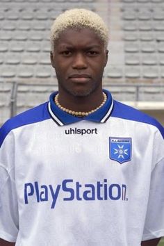 a man standing in front of a soccer field wearing a white and blue uniform with the word play station on it