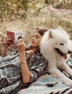 a woman laying on the ground reading a book with a white dog sitting next to her