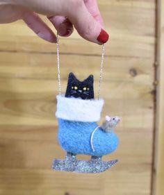 a hand holding a small felt ornament with a cat on it's back