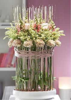 a vase filled with lots of flowers sitting on top of a white table next to a candle