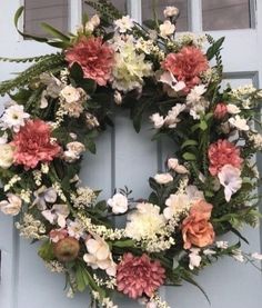 a wreath is hanging on the front door with flowers and greenery around it,