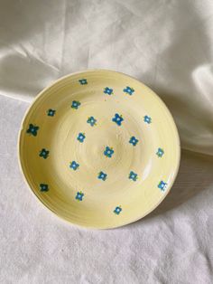 a yellow bowl with blue flowers on it sitting on a white cloth covered tablecloth