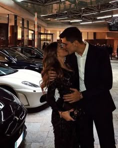 a man and woman kissing in front of some cars