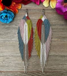 two pairs of multicolored fringe earrings on wooden surface with flowers in the background