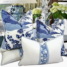 two blue and white pillows sitting on top of a table next to vases with flowers