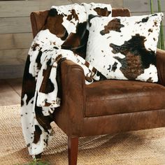 a cow print throw blanket sitting on top of a brown chair next to a plant