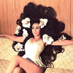 a woman laying on top of a bed with flowers in her hair and long black hair