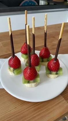 there are strawberries and kiwis on the white plate with toothpicks