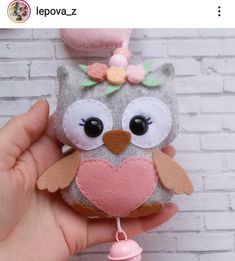 a hand holding a small stuffed owl with a pink heart