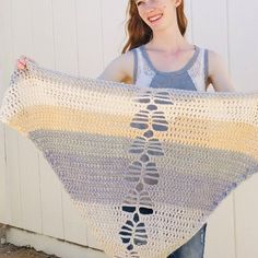 a woman holding up a crocheted shawl in front of a white wall