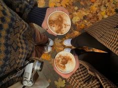 two people holding cups of coffee in their hands with autumn leaves on the ground behind them