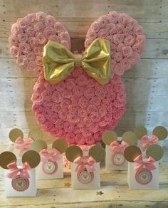 a minnie mouse cake with pink roses and gold bow on it, surrounded by small gift bags