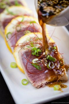 someone pouring sauce on some food on a plate