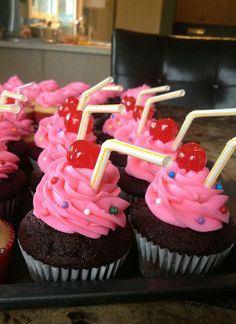 cupcakes with pink frosting and cherries on sticks are sitting on a tray