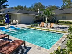 an empty swimming pool surrounded by lawn chairs and umbrellas in front of a house