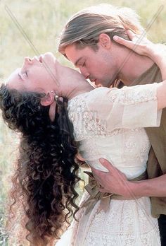 a man and woman kissing in the middle of an open field with tall grass behind them