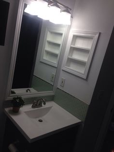 a white sink sitting under a bathroom mirror next to a shelf with books on it