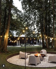 a fire pit surrounded by chairs and lights in the middle of a yard with lots of trees