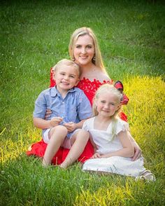 a woman and two children are sitting in the grass smiling at the camera while posing for a family photo