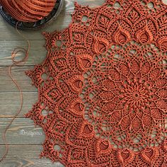 an orange crocheted doily next to a ball of yarn on a wooden table