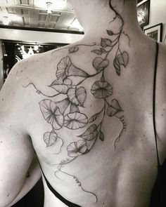 the back of a woman's shoulder with flowers and leaves tattoo on her left side