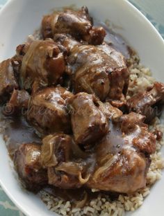 a white bowl filled with rice and meat covered in gravy on top of a table