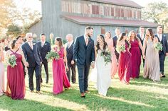 a large group of people standing in front of a barn wearing formal clothes and holding bouquets