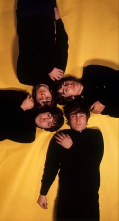 the beatles are standing in a circle on a yellow sheet with their arms around each other