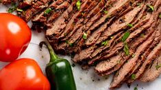 sliced flank steak with tomatoes and green peppers on the side, ready to be served