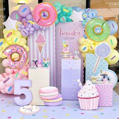 a table topped with lots of balloons and donuts next to a sign that says happy 5th birthday