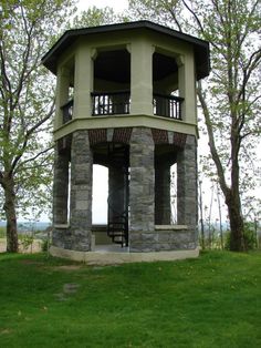 a small tower sitting on top of a lush green field next to trees and grass