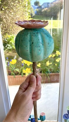 a hand is holding a blue and green glass candle holder in front of a window