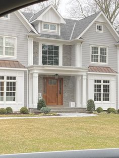 a large gray house with white trim and brown doors is seen from the car window