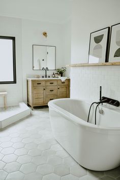 a large white bath tub sitting next to a sink in a bathroom under two framed pictures