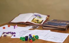 dices and books on a table with paper work in the foreground, including an open book