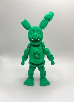 a green toy that looks like an alien with two hands on his chest and one hand in the air