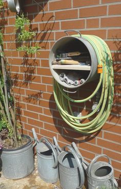 several buckets and gardening tools are on the ground next to a brick wall with a garden hose hanging from it