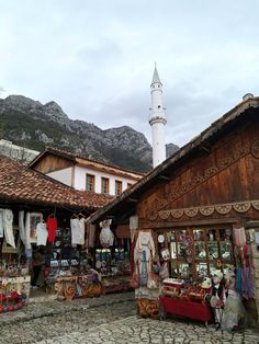 an outdoor market with people shopping in front of it and a tall white tower behind them