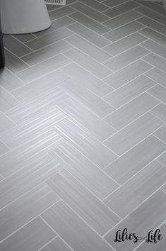 a bathroom with white tile floors and a toilet in the corner, next to a trash can