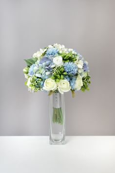 a clear vase filled with blue and white flowers on top of a table next to a gray wall