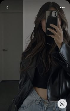 a woman taking a selfie while wearing a leather jacket and silver pants with her cell phone up to her ear