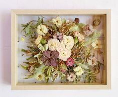 an arrangement of flowers is displayed in a wooden frame on the wall above a mirror