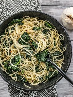 a bowl filled with pasta and spinach on top of a table next to garlic