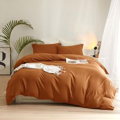 a bed with an orange comforter in a white room next to a potted plant