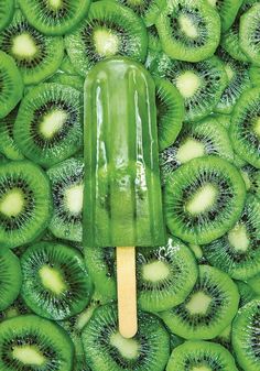 a green popsicle with kiwi slices on it is in front of a background of sliced kiwis