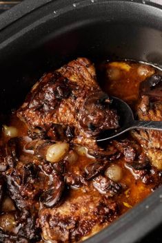 the meat is being cooked in the slow cooker with a spoon and some onions