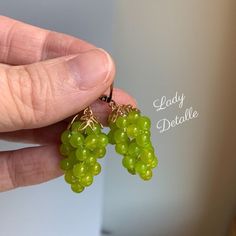 a person is holding some green grapes in their left hand and the other one has gold earwires