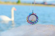 a small clock is hanging on a rock near the water with swans in the background